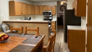 A compact kitchen with wooden cabinets, a microwave, a refrigerator, and a dining area with a table and chairs. - 5BR Recently Updated Retreat w/ Hot Tub, BBQ grill, Fire Pit, Near Attractions (Colorado Springs)