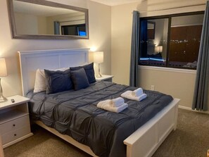 A neatly made bed with a dark quilt, two pillows, and two towels on the side. - Spacious 5BR 4-Bath Retreat with 600 sq ft private 150" 4K Dolby Cinema & Lounge (Colorado Springs)