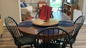 Ein Essbereich mit einem runden Tisch, schwarzen Stühlen und einer Chandelier. Im Hintergrund befindet sich eine Couch und ein Fernseher.