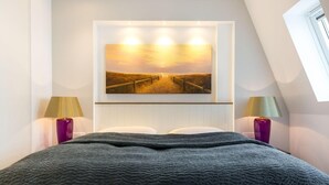 A bedroom with a large bed, two bedside lamps, a wall-mounted painting, and a window. - Art your Life - Residence, Whg. 11 Superdet - Art your Life - Residence Seeburg (Sylt)