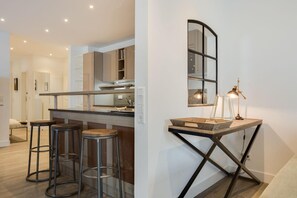 A modern kitchen with a bar area, stools, and a unique wall-mounted lamp.