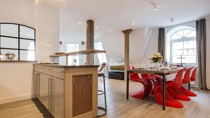 A modern kitchen with a central island, a dining area with red chairs, and a large window providing natural light. - Art your Life - Residence, Whg. 11 Superdet - Art your Life - Residence Seeburg (Sylt)