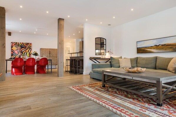 A modern living room with a sofa, a coffee table, and a dining area with red chairs.