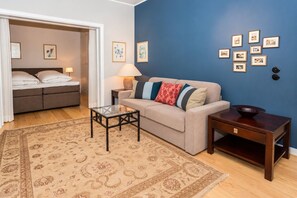 A room with a sofa, a glass coffee table, a side table with a bowl, a patterned rug, and a bed with a headboard. - Villa Maybach, Whg. 1 Albert - Villa Maybach (Sylt)