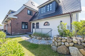 A two-story house with a brick facade, a stone pathway, and a small garden with rocks and plants. - Villa Maybach, Whg. 1 Albert - Villa Maybach (Sylt)