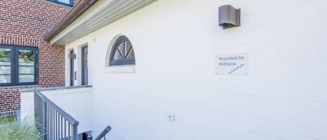 A building exterior with a white brick wall, a metal staircase, and a sign reading "Waschküche Wellness".