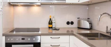 Una cocina moderna con armarios blancos, horno empotrado, microondas, tostadora y pileta.