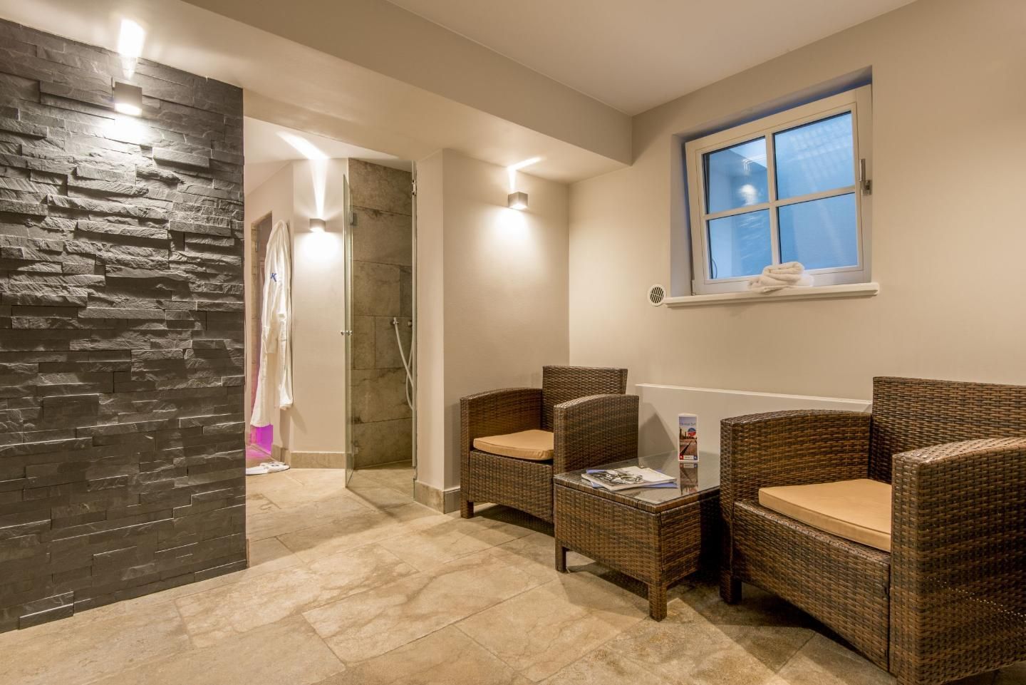 Uma área de spa com cadeiras de vime, uma mesa de vidro, uma parede de pedra e um espaço com chuveiro.