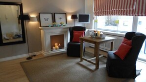 Un salon avec une cheminée, deux fauteuils, une petite table et un téléviseur.