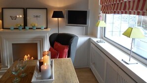 Un salon chaleureux avec une cheminée, un téléviseur et une fenêtre ornée de rideaux à rayures.