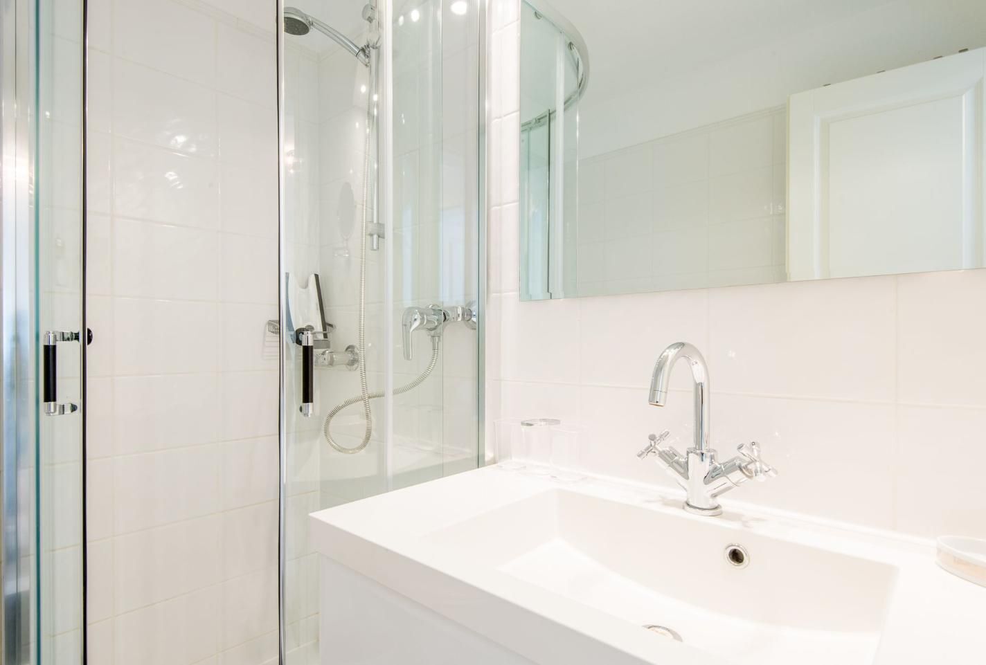 A modern bathroom with a glass-enclosed shower, a white sink with a single faucet, and a large mirror above the sink.