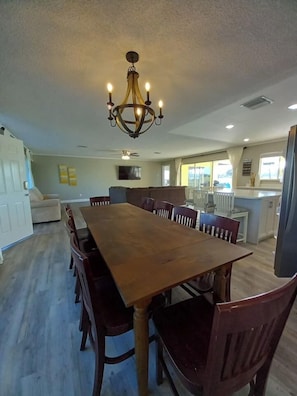 Zona pranzo con tavolo e sedie in legno, un lampadario e una cucina sullo sfondo.