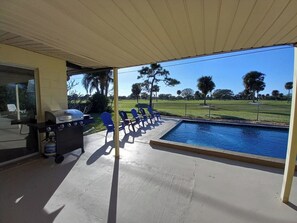 Una veranda riparata con piscina, zona barbecue e sedie blu.