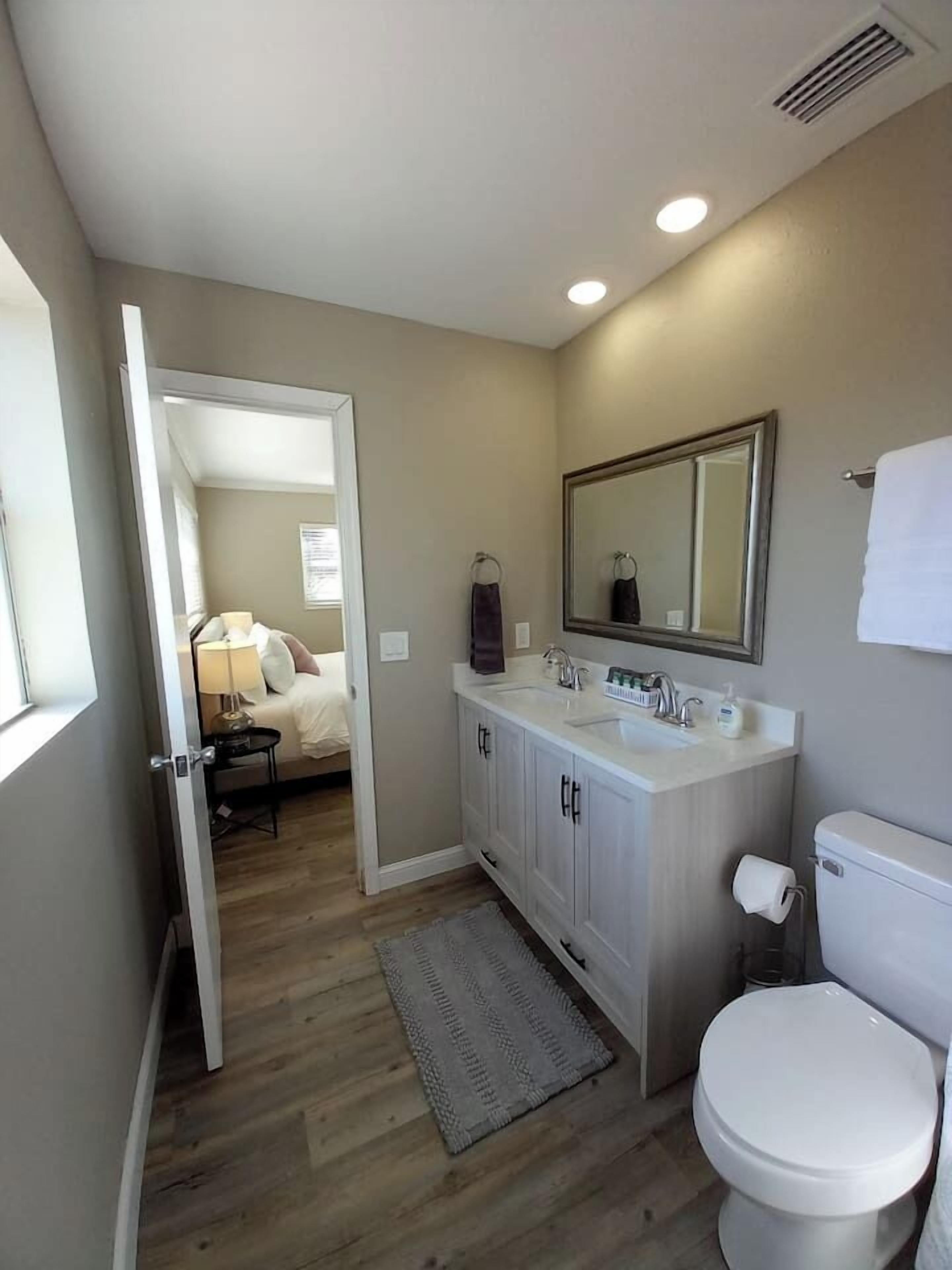 Un baño con inodoro blanco, lavamanos con espejo y suelo de madera.