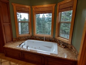 Une salle de bain avec une grande baignoire, trois fenêtres à cadre en bois et un pare-baignoire carrelé.