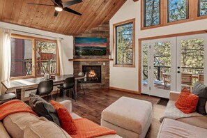 Una sala de estar acogedora con chimenea, techo de madera y grandes ventanas con vistas a una terraza.