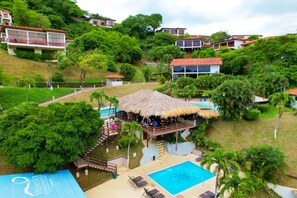 Un complexe hôtelier doté d’une piscine, d’une structure à toit de chaume et de plusieurs bâtiments situés sur une colline.