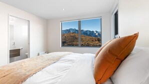 Une chambre avec un lit, une fenêtre donnant sur la montagne, une salle de bain avec un lavabo et des toilettes, et une porte.