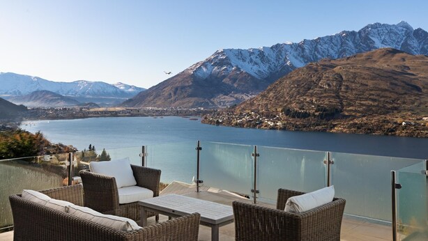 Un balcon meublé avec des meubles en osier, donnant sur un lac et des montagnes.