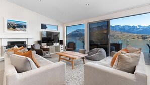 Un salon moderne doté d’une grande fenêtre offrant une vue sur les montagnes, d’un téléviseur à écran plat et de sièges confortables.