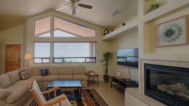 A living room with a sectional sofa, a wooden chair, a coffee table, a fireplace, a TV, and large windows. - Quiet Home Close to Sedona (Rimrock)