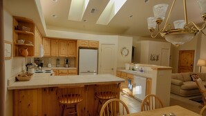 A kitchen with wooden cabinets, a central island with stools, a refrigerator, and a dining area with a table and chairs. - Quiet Home Close to Sedona (Rimrock)