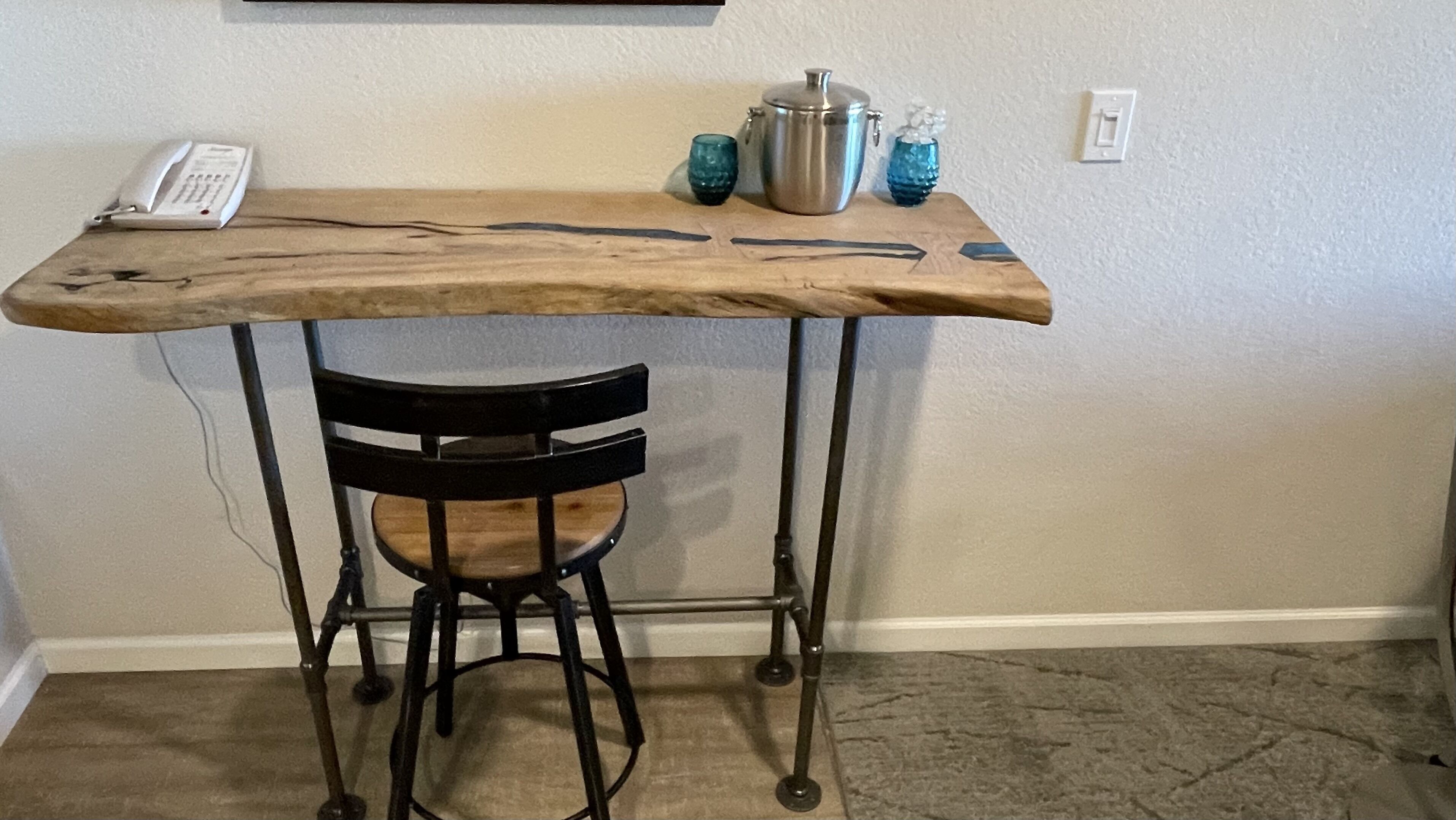 A small wooden table with a metal frame, a black chair, and a phone on the table.