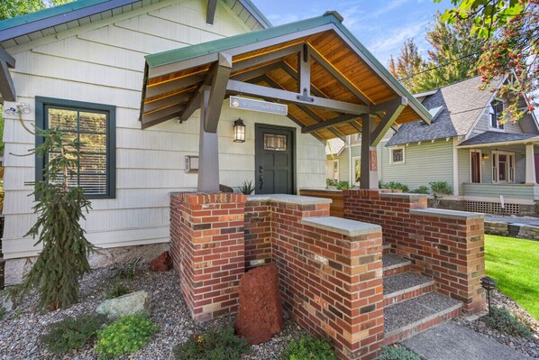 A house with a covered porch, a brick fireplace, and a front door. - Downtown Craftsman with King Bed and Private Yard - Walk Everywhere (Bend)