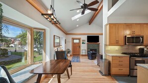A spacious kitchen with wooden cabinets, a microwave, and a stove. There is a dining area with a table and chairs, and a large window providing a view of the outdoors. - Downtown Craftsman with King Bed and Private Yard - Walk Everywhere  (Bend)