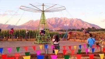 A carousel with a mountainous backdrop, surrounded by people and colorful flags.