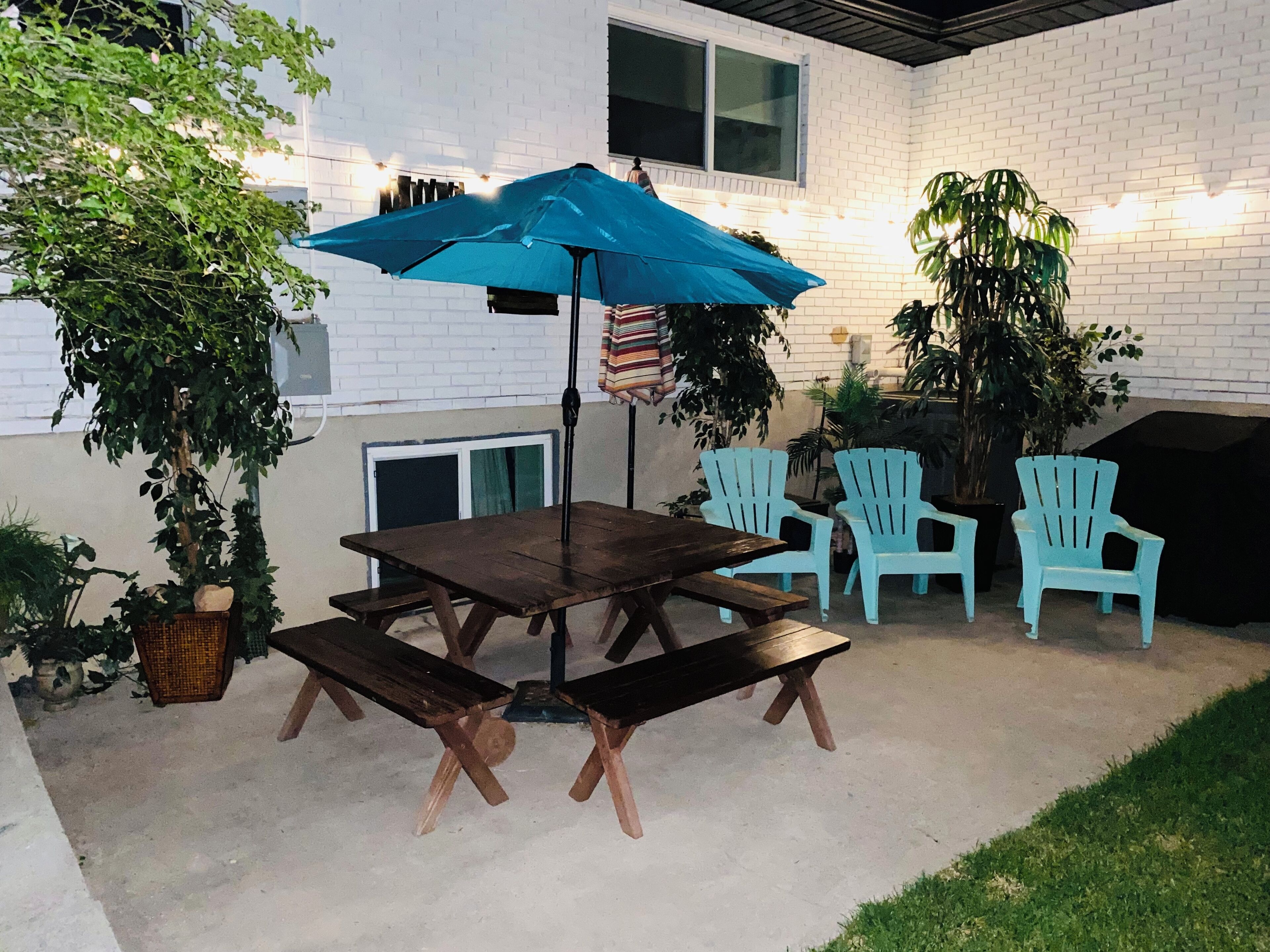 Eine Terrasse mit Holztisch und -stühlen, einem blauen Sonnenschirm und Topfpflanzen.