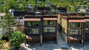 A modern multi-story building with large windows, a flat roof, and a view of a forested hillside.