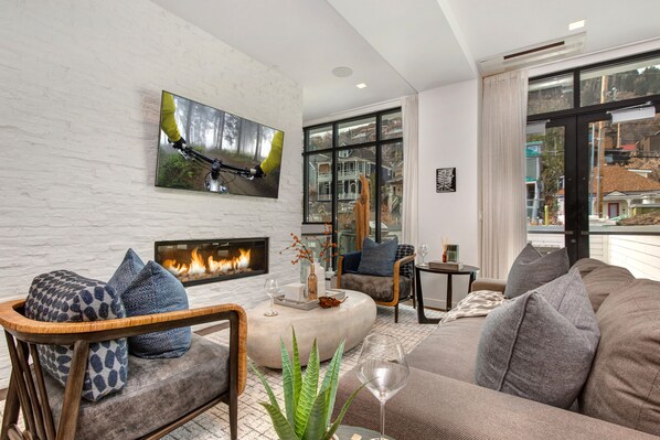 A modern living room with a fireplace, comfortable seating, and a large window offering a view of the neighborhood.
