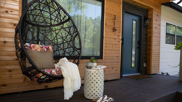A wooden exterior with a number '318' on the door, a hanging chair with a cushion, a small table with a plant, and a pair of sandals on the deck.