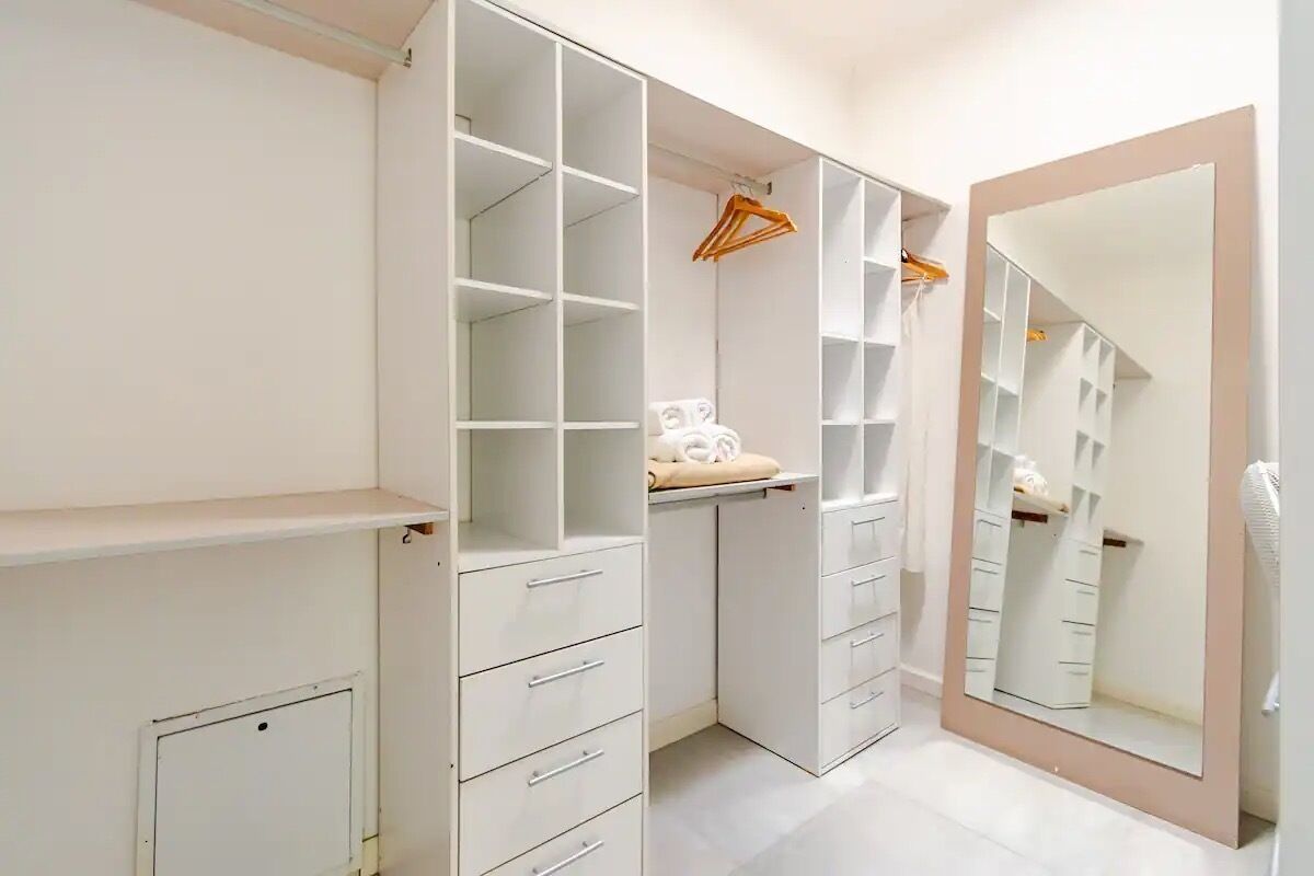 Un dressing accessible sans porte, doté d’étagères ouvertes, d’un miroir et d’une tringle pour suspendre les vêtements.