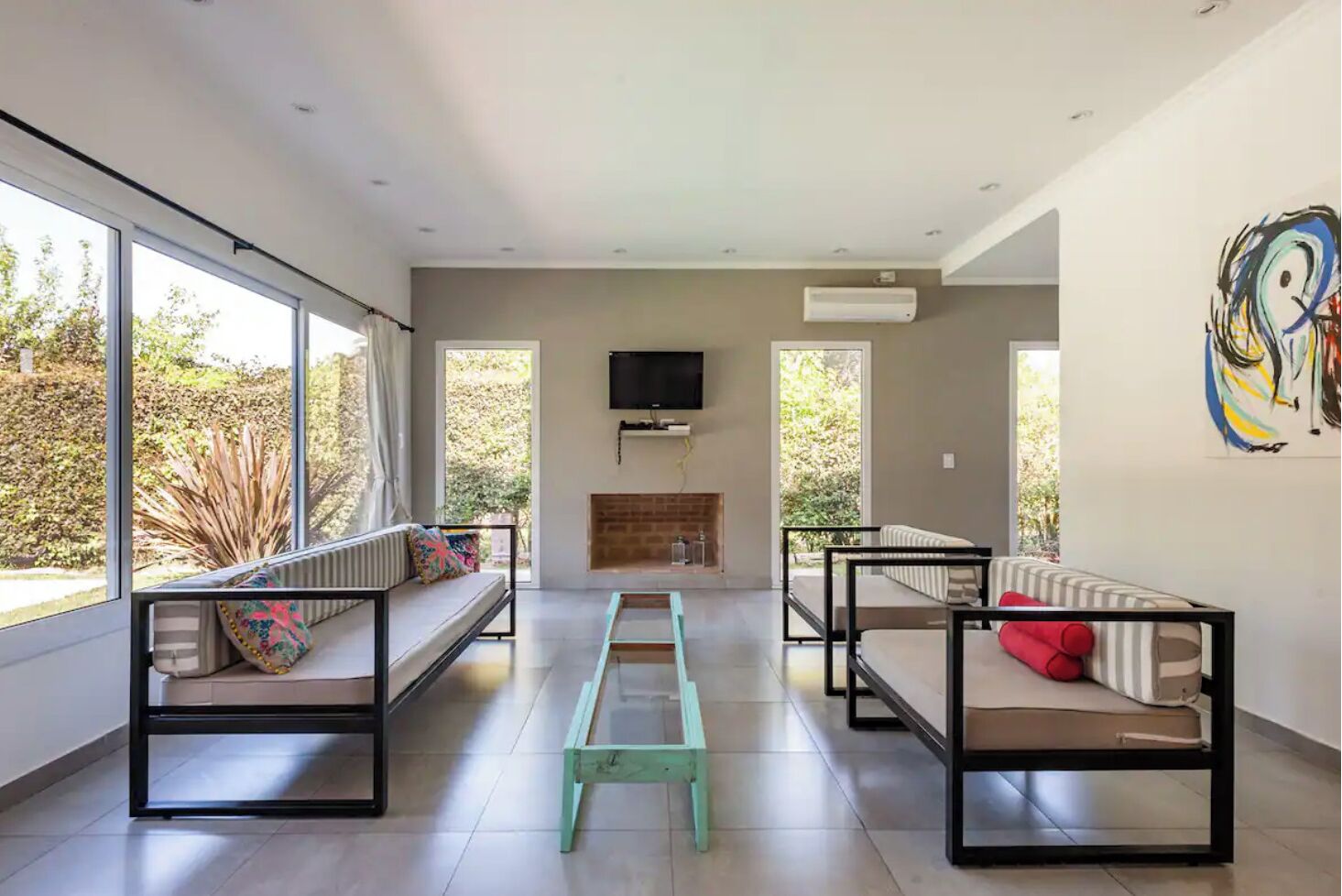 A modern living room with large windows, a fireplace, and a TV.