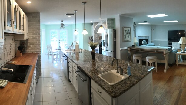 A modern kitchen with granite countertops, white cabinetry, and a central island with seating. - OCEAN BREEZE IS A LUXURY GETAWAY THAT HAS IT ALL (Ormond Beach)