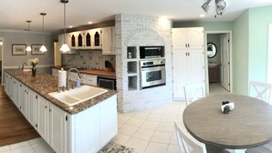 A kitchen with granite countertops, white cabinets, a stone backsplash, and a dining area with a round table. - OCEAN BREEZE IS A LUXURY GETAWAY THAT HAS IT ALL (Ormond Beach)