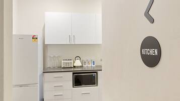 A modern kitchen with white cabinets, a microwave, a toaster, and a kettle. There is a 'KITCHEN' sign on the wall.