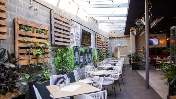 An outdoor cafe with white chairs and tables, potted plants, and a mural on the wall. - Padstow Park Hotel (Padstow)