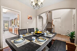 Un coin repas avec une longue table dressée pour six personnes, entourée de chaises, et un panier de fruits posé sur la table.