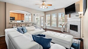 A spacious living room with a white sectional sofa, a fireplace, and a television mounted on the wall.