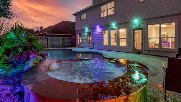 A swimming pool with a hot tub, surrounded by a wooden fence and palm trees.