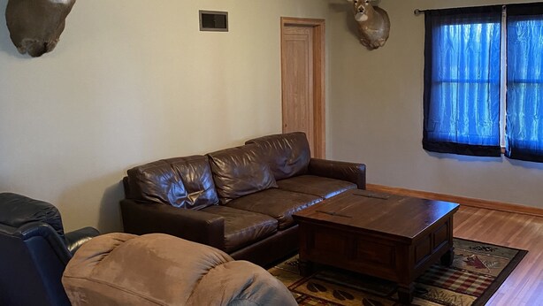 Ein Wohnzimmer mit einem braunen Ledersofa, einem Holztisch und zwei Hirschgeweihen an der Wand.