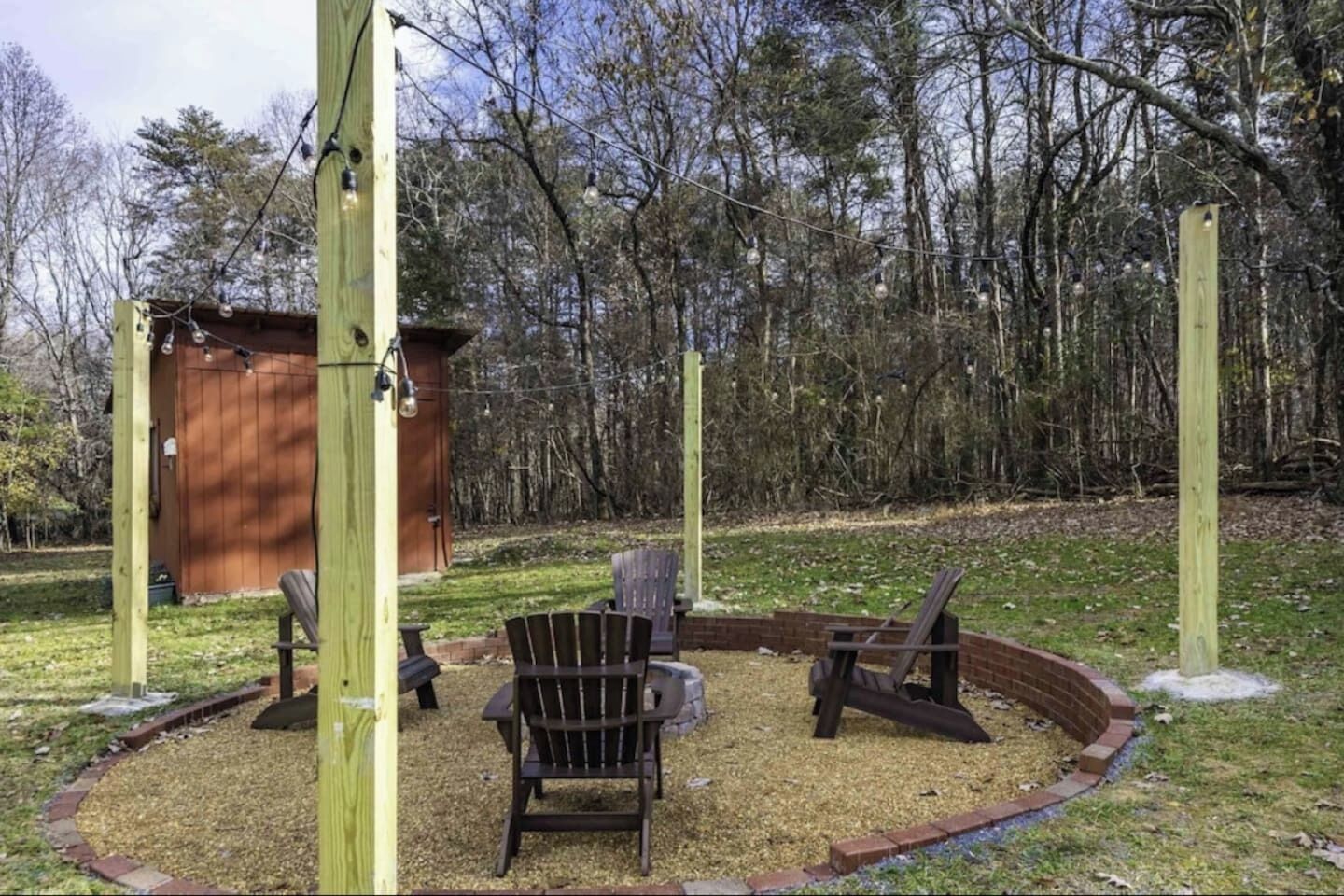 A wooden deck with Adirondack chairs and a fire pit in a wooded area.