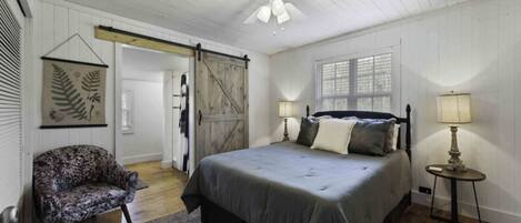 Ein Schlafzimmer mit Bett, Stuhl, Lampe, Deckenventilator und Fenster.