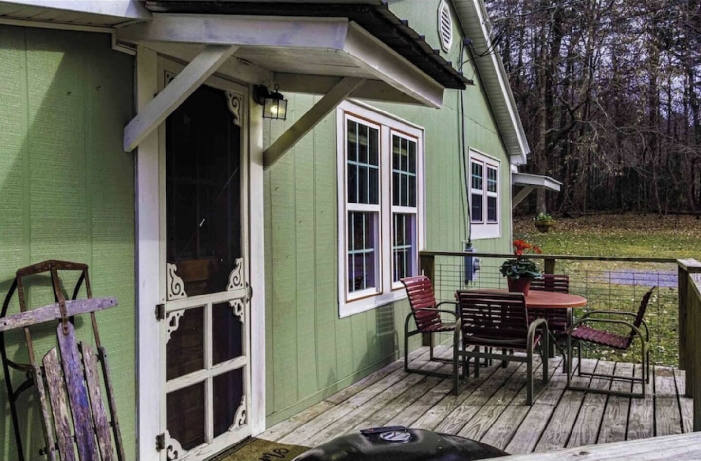 Une maison verte avec une terrasse en bois, une porte et une fenêtre.