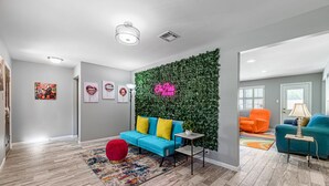A modern living room with a blue sofa, red ottoman, and a green wall with a neon sign. - The Paris- Colorful 3BEDROOM 2BATH SFH w/Heated POOL Available  (Houston)
