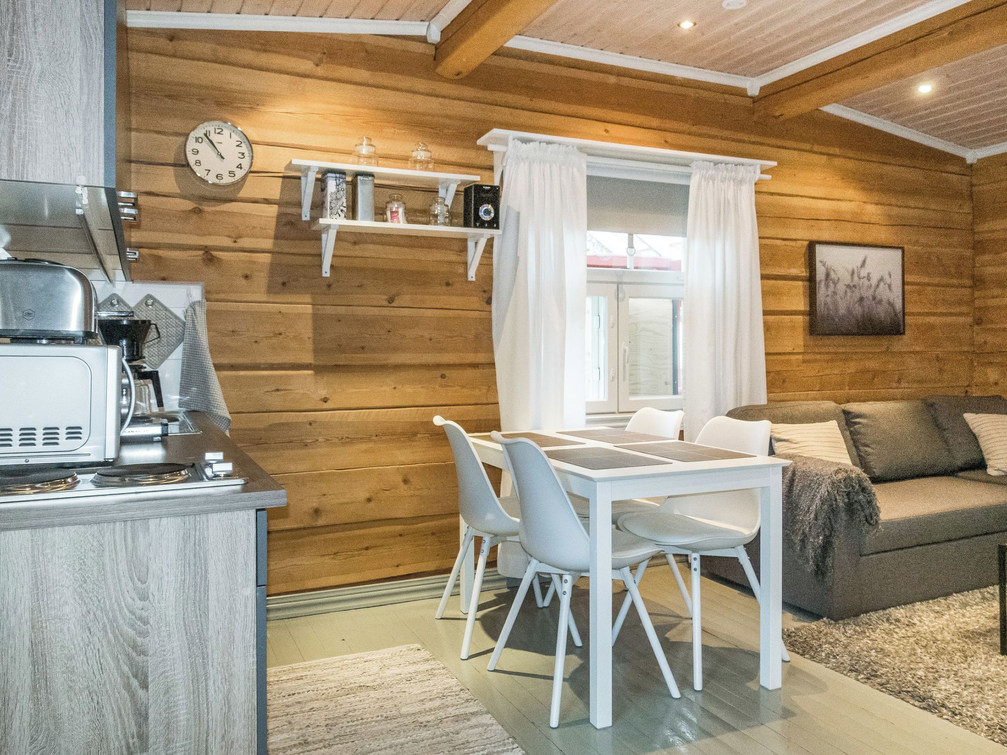 A compact kitchen with a stove and a microwave, a dining table with chairs, and a sofa in a room with wooden walls.