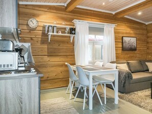 A compact kitchen with a stove and a microwave, a dining table with chairs, and a sofa in a room with wooden walls.